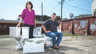 a man and a woman posing with toilets in a parking lot